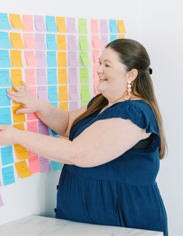 Laura sticking a sticky note onto a colorful sticky note wall