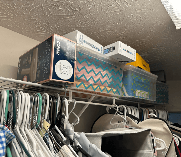 A bedroom closet with clutter on the top shelf and organizers not being used properly