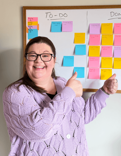 Laura pointing to a baord with sticky notes on it, some on a side that says "to-do" and the others under "done"