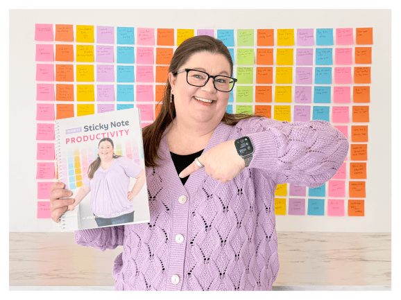 Laura holding the guide to Sticky NOte Productivity in front of a wall covered in colorful sticky notes
