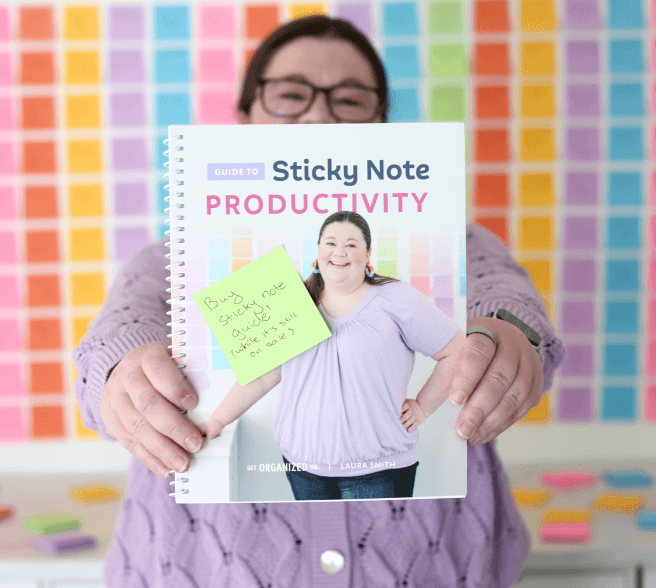 Laura holding the guide to Sticky NOte Productivity in front of a wall covered in colorful sticky notes