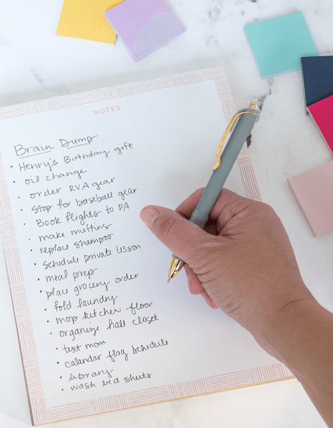 someone writing a brain dump on a notepad next to aticky notes