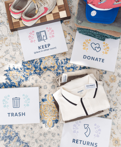 4 signs on the floor lableing piles of clothes and items with "Keep", "Donate", "Trash", and "Returns"